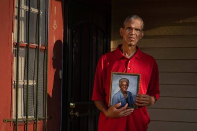 A man wearing a red shirt holding a photo of his mother.