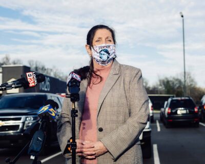 Dr. Alisa Haushalter, wearing a mask and speaking in front of press microphones.