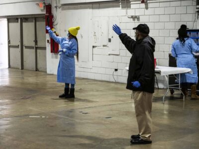 Workers wave in a line of cars with people receiving the COVID-19 vaccine.