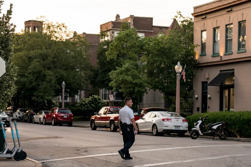 A man in a white shirt and black pants crosses a crosswalk in a residential neighborhood.