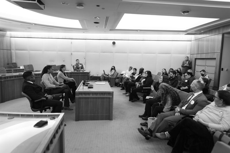 Three people sit at a desk in a hearing room.