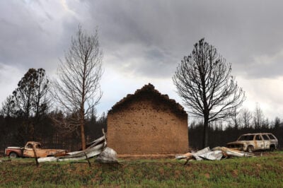 A brick wall, scorched at the top, sits between two burned cars.