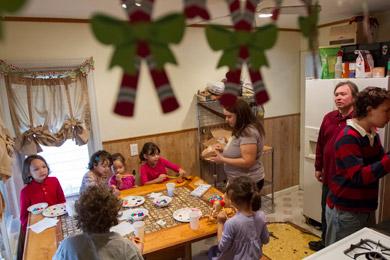 Claire Rembis, who home schools her nine children, leads them in an arts project as her husband Willie, 44, looks on from in front of the refrigerator. (Jeffrey Sauger for ProPublica)